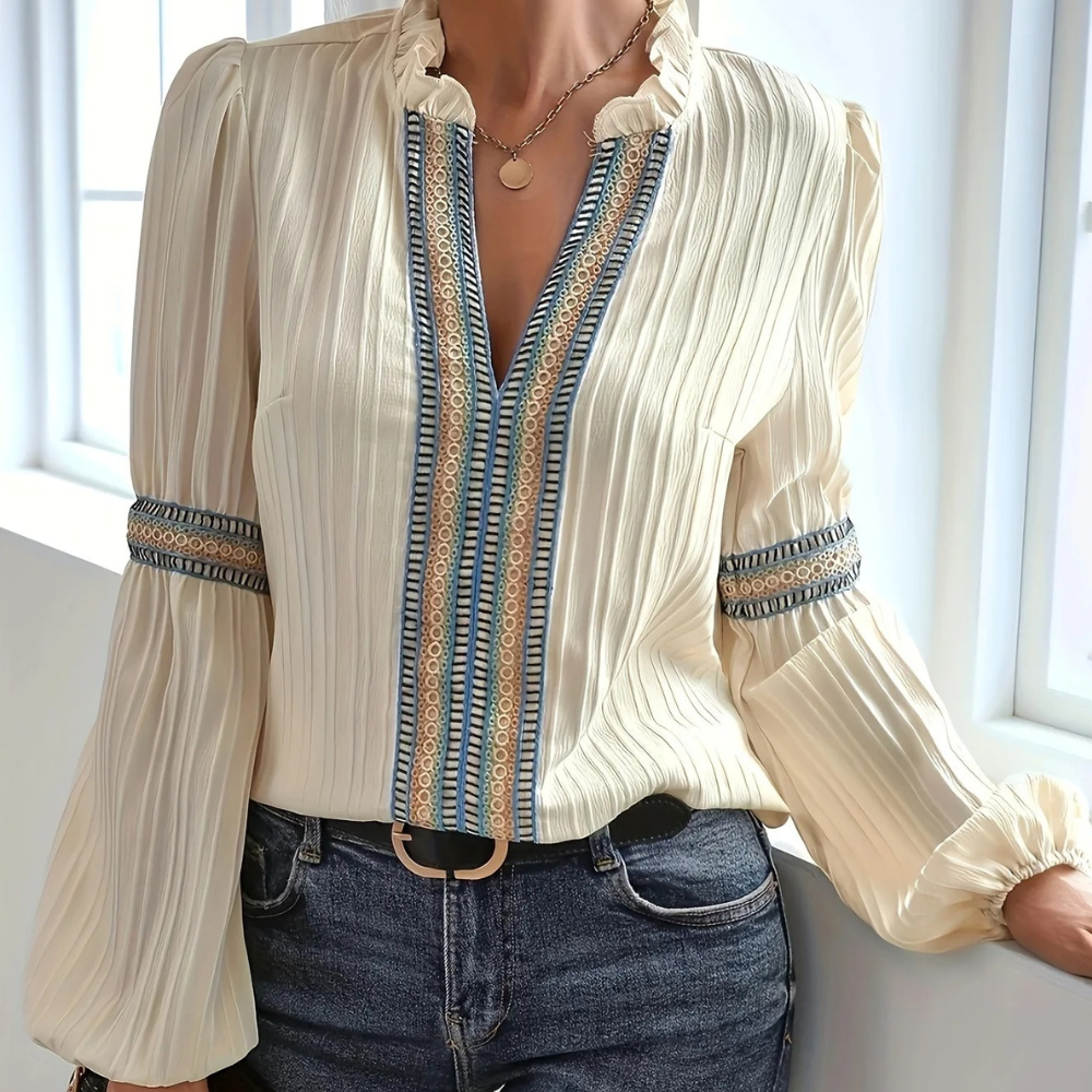 Vrouw in stijlvolle crèmekleurige blouse met blauwe en gouden details, geplooide mouwen, gecombineerd met spijkerbroek. Elegante damesmode.