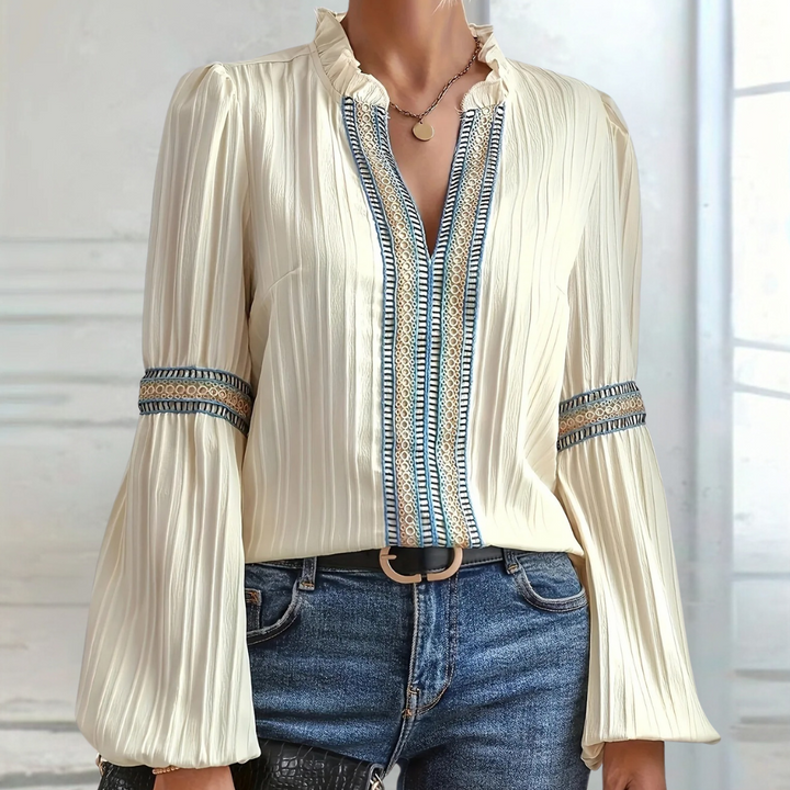 Elegante crèmekleurige blouse met lange mouwen, geplooide stof en blauwe borduursels, gedragen met spijkerbroek. Perfect voor modieuze damesoutfits.