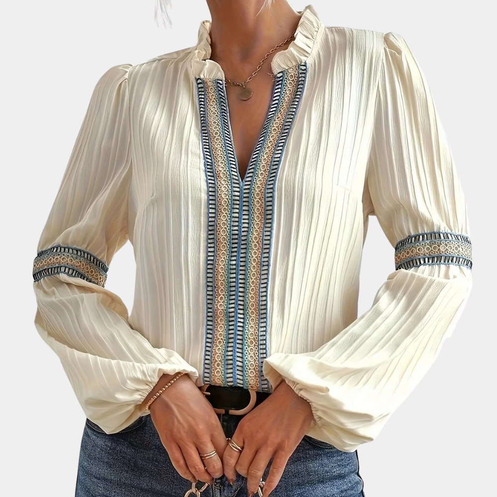 Crèmekleurige blouse met lange mouwen, geplooide stof en blauwe borduursels, gedragen door een model. Perfect voor modieuze damesoutfits.