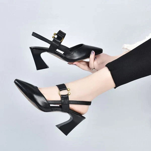 Elegante zwarte leren pumps met blokhak en gouden details, gedragen door vrouw. Modieuze damesschoenen, perfect voor formele gelegenheden.