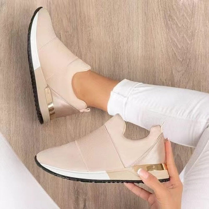 Beige dames sneakers met gouden details, comfortabele pasvorm, gedragen met witte broek op houten vloer. Trendy en stijlvol schoeisel.