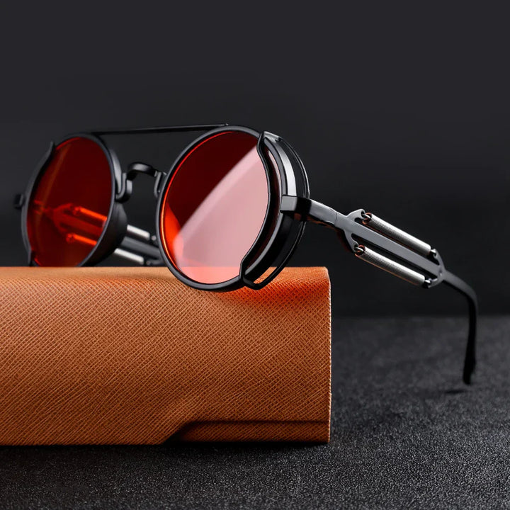 Ronde zonnebril met rode glazen en zwart metalen montuur op een oranje etui, stijlvolle unisex zonnebril, retro design, UV-bescherming.