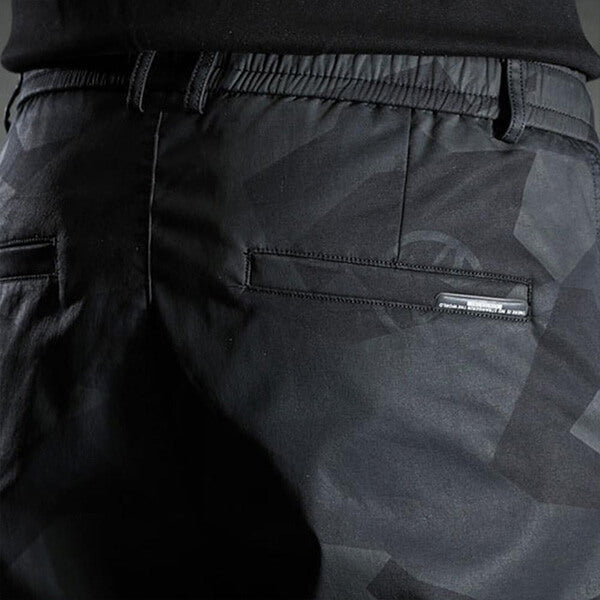 Zwarte camouflagebroek met elastische tailleband en achterzakken, geschikt voor casual en outdoor activiteiten. Comfortabele pasvorm, trendy design.